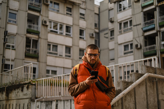 Portrait of man in orange vest with smartphone in hand, standing on urban staircase - Powered by Adobe