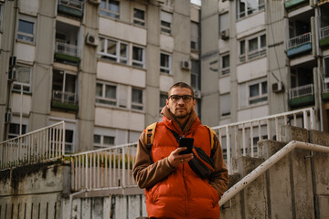 Portrait of man in orange vest with smartphone in hand, standing on urban staircase