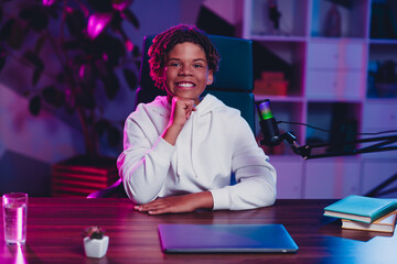 Young man with a microphone sitting indoors, engaging in online blogging or streaming, illuminated by colorful neon lighting