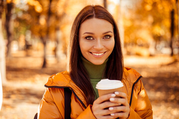 Charming young woman enjoying coffee in an autumn park surrounded by vibrant foliage during a...