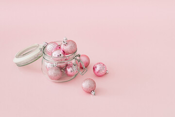 Christmas composition made with jar full of pink Xmas baubles on pastel pink background. Minimal...