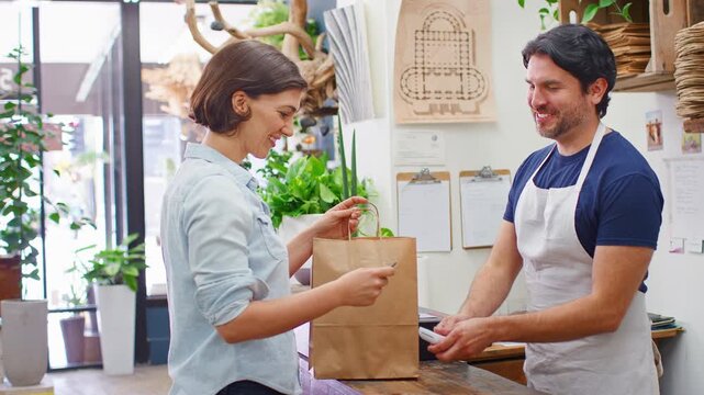 Woman In Florists Store Making Contactless Payment At Sales Desk Holding Credit Card To Reader
