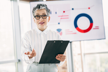 Professional businesswoman giving a presentation with charts, confidently addressing colleagues during an office meeting
