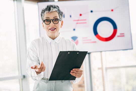 Professional businesswoman giving a presentation with charts, confidently addressing colleagues during an office meeting
