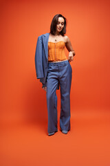Fototapeta premium Chic young woman in blue suit and corset poses against an orange background
