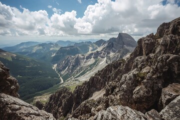 Fototapeta premium Scenic mountain valley showcasing towering cliffs and misty clouds, ideal for hiking and climbing in warm weather.