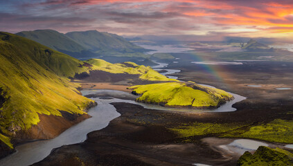 Aerial view of Iceland's moss covered hills, winding rivers, volcanic terrain, and scattered lakes, with a rainbow arching over the landscape.