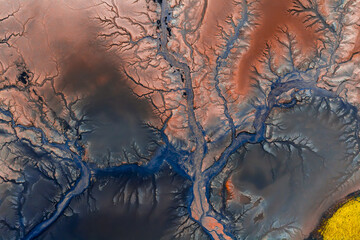 Aerial image of blue streams weaving through reddish brown terrain in Iceland, with a bright yellow patch and volcanic formations visible.