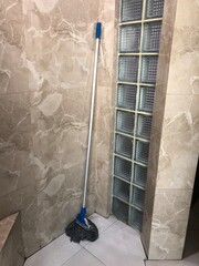 Mop leaning against tiled wall in bathroom corner