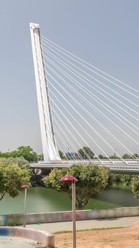 Alamillo Bridge with a tall pylon and steel cables spans over the Guadalquivir River in Seville, Spain. Timelapse hyperlapse of modern suspension design with busy traffic under a clear blue sky.