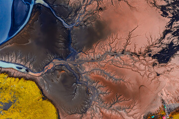 Aerial image of Iceland showing branching river channels, red and black sediment, yellow moss, and a blue lake in the upper left corner.