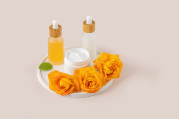 Skincare product display with cream jar, serum bottle and yellow rosebuds. Perfect for...