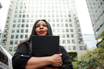 Businesswoman holding laptop and looking up at buildings in canary wharf, london