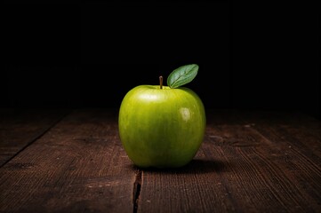 A vibrant green apple resting on a wooden table, set against a dark backdrop.