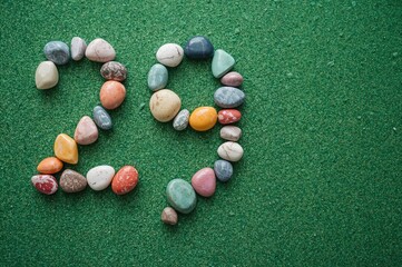 Calendar date of 29 June arranged with colorful stones on a green sandy surface, design concept for birthday celebration