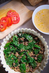 Making homemade french quiche with spinach, meat, tomato, and cheese