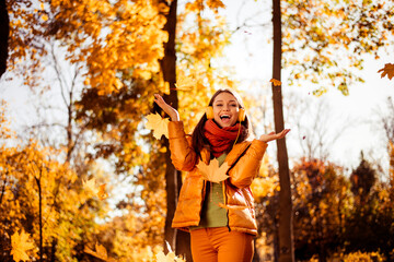 Young woman enjoying an autumn day outdoors surrounded by golden leaves in a park, radiating joy and style