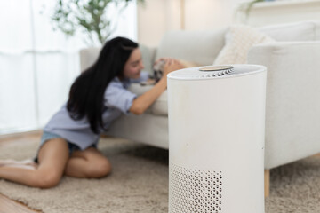 Modern air purifier in cozy living room with blurred Asian woman playing with dog in background....