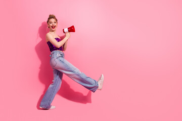 Attractive young woman with a megaphone posing against pink background promoting a cheerful lifestyle in stylish attire