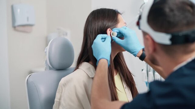 An otolaryngologist examines a patient. The doctor examines the ear of a young woman using special instruments.