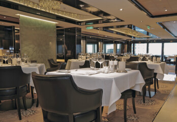 Formal elegant restaurant dining room onboard luxury cruiseship or cruise ship liner with set tables, ocean views and impressive interior inside architecture chandelier