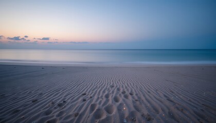 Fototapeta premium Serene ocean horizon with patterned sandy beach under soft pastel sky during twilight