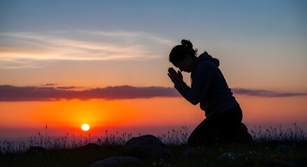 Silhouette of a woman kneeling in prayer during a vibrant sunset, the fiery colors of the sky reflecting her peaceful devotion.