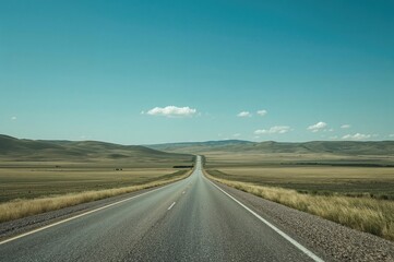 Expansive road running through open grassland under a clear blue sky