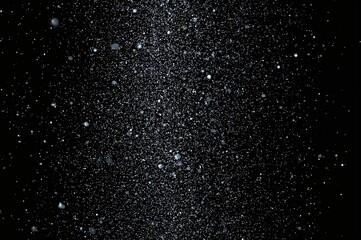 Photo of snowflakes descending, varying in size from large to small, captured in midair on a dark background.