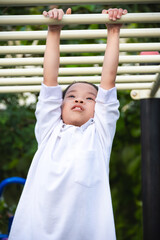 Portrait of happy young girl hanging on monkey bars at outdoor playground in summer park. Asian...