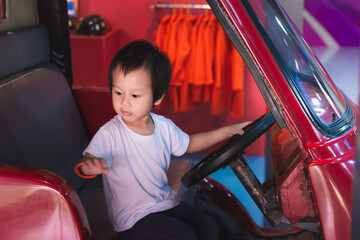 Portrait of a happy little boy sitting at the steering wheel of a red model car or fire truck,...