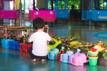 Back view of a happy little boy playing pretend, taking care of a vegetable garden, watering can...