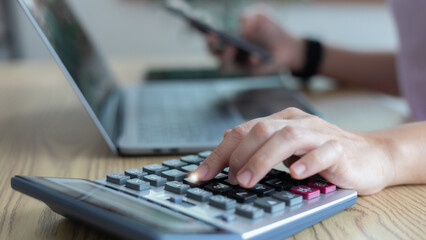 Hand using a calculator with a laptop and smartphone for finance and accounting. Concept of budget...