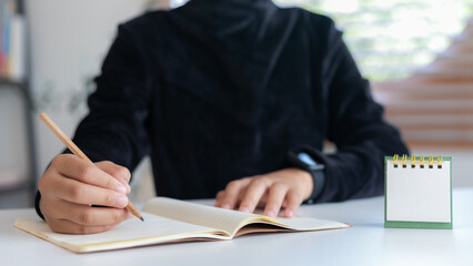 Close-up of handwriting on a notebook with a pencil and a blank desk calendar. Concepts of...