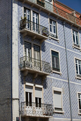 Lisbon, Portugal - Blue and white building with a balcony. The balcony has a railing and a potted plant