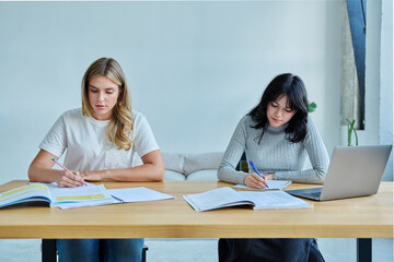 Two university students sitting at desk studying, with laptop, textbooks, notebooks