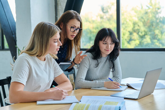 Two university student girls with female teacher mentor study while sitting at desk