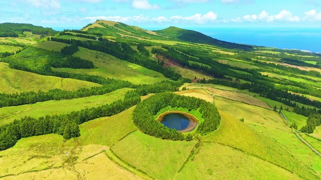 Lake Pau Pique and Lush Green Hills with Pastureland and Trees. Atlantic Ocean. Moving Shadows from Clouds. Azores, Sao Miguel Island. Portugal. Aerial View. Drone Moves Forward