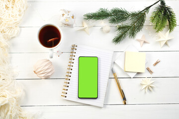 Notepad, pen, cup of tea, for writing plan or Christmas wish list. Phone with green screen on...