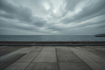 Intense shoreline view featuring a solid concrete wall, paved area, vast water expanse, and cloudy sky