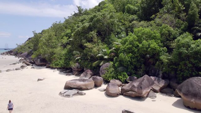 Drone footage of cap ternay beach, near granite stone and trees at low tide, Single woman walking towards the granite rocks, Mahe, Seychelles 30fps 4
