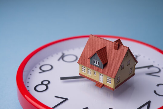 House model on analog round clock with blue background copy space. Time to repayment mortgage loan, due date installment, pay house rent and deadline pay others expenses and so on concept.
