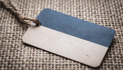 A rustic blank price tag or label with a blue and white diagonal split tied with twine resting on a textured burlap background perfect for product branding or retail