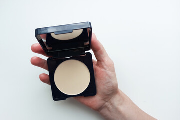 Compact powder in a black powder box in the hand of a Caucasian woman. White background.