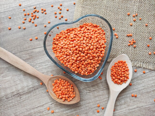 Dried small red lentils in a decorative plate and wooden spoons on a wooden background