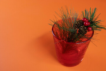 A Christmas red berries bouquet in a red glass on Orange background