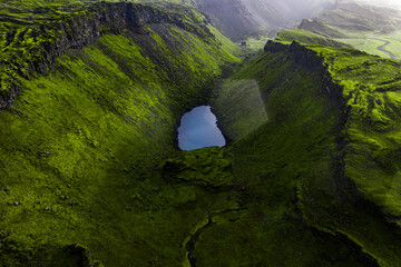 Lush green volcanic crater in Iceland with moss covered walls, a reflective lake at its center, and...