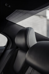 Rear leather seat headrest in a car. Sedan interior with black leather seats, unfocused concrete...