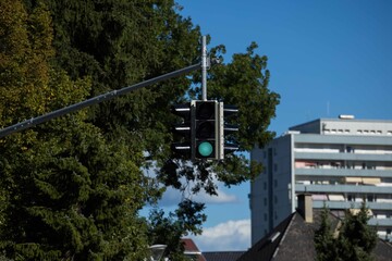 Urban traffic light displaying green signal against blue sky with trees and buildings