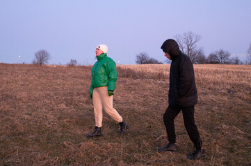 Two figures walk across a sprawling field during twilight, enjoying the last light of day while...